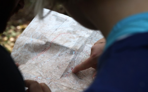 Two people outdoors pointing a map that one person is holding